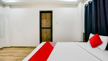 A hotel room with a wooden door, a bed with white bedding and a red pillow, and a dark curtain.