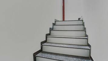 A staircase with a handrail and a red pipe running vertically along the wall.