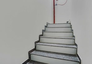 A staircase with a handrail and a red pipe running vertically along the wall. - Hotel O White Villa (, Nagpur)