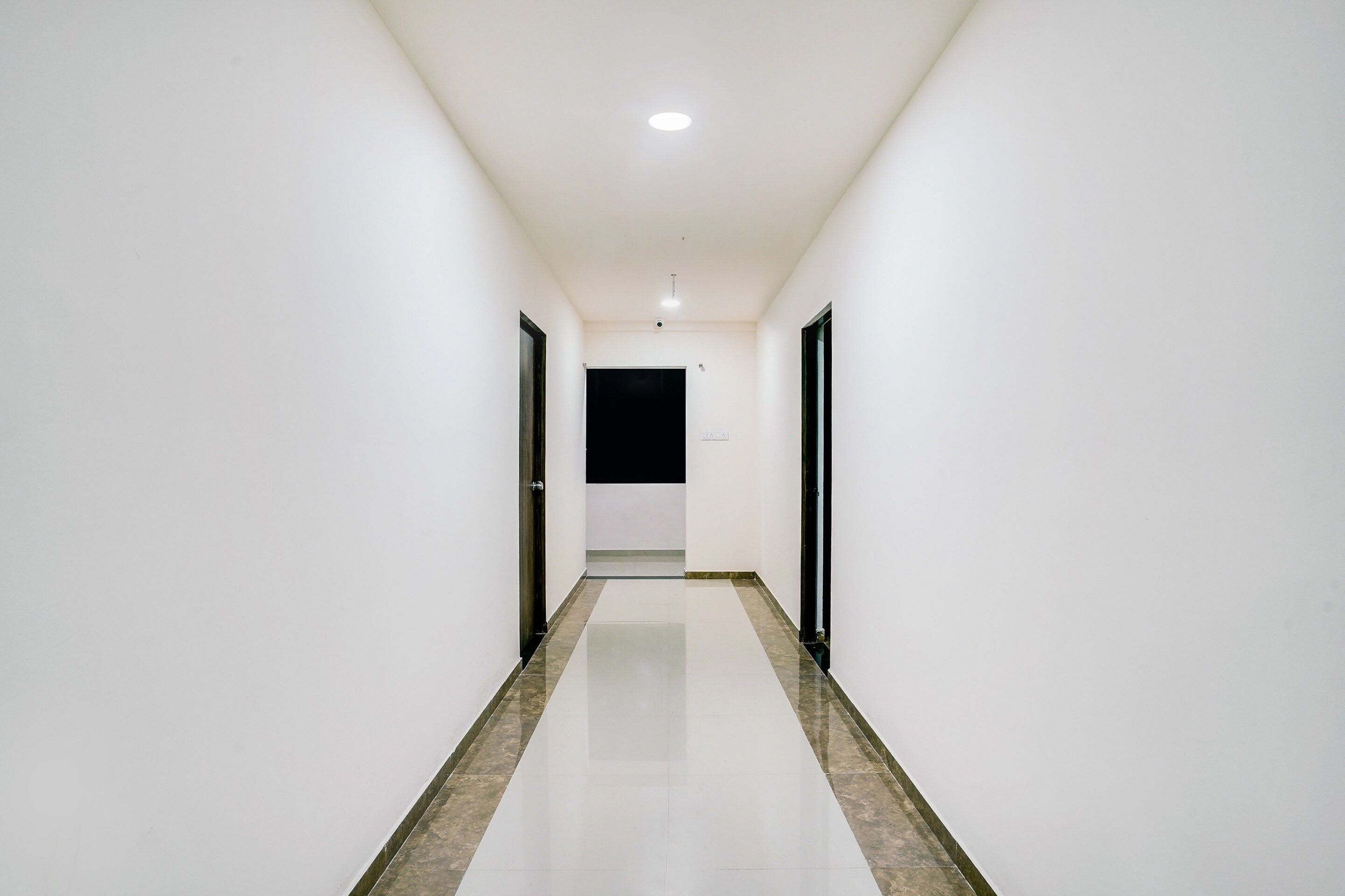 A corridor with white walls and a shiny floor, leading to a door at the end.