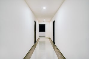 A corridor with white walls and a shiny floor, leading to a door at the end. - Hotel O White Villa (, Nagpur)