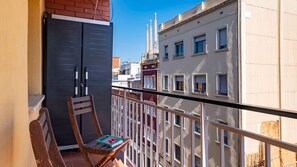 Ein Balkon mit Stuhl und Buch, mit Blick auf eine Stadtlandschaft mit Gebäuden und blauem Himmel.