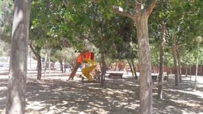 Ein Spielplatz mit einer gelben Rutsche und einer roten Kletterattrappe, umgeben von Bäumen.