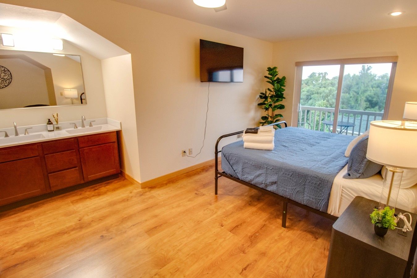 Un dormitorio con cama, mesita de noche, ventana y baño con lavamanos y espejo.