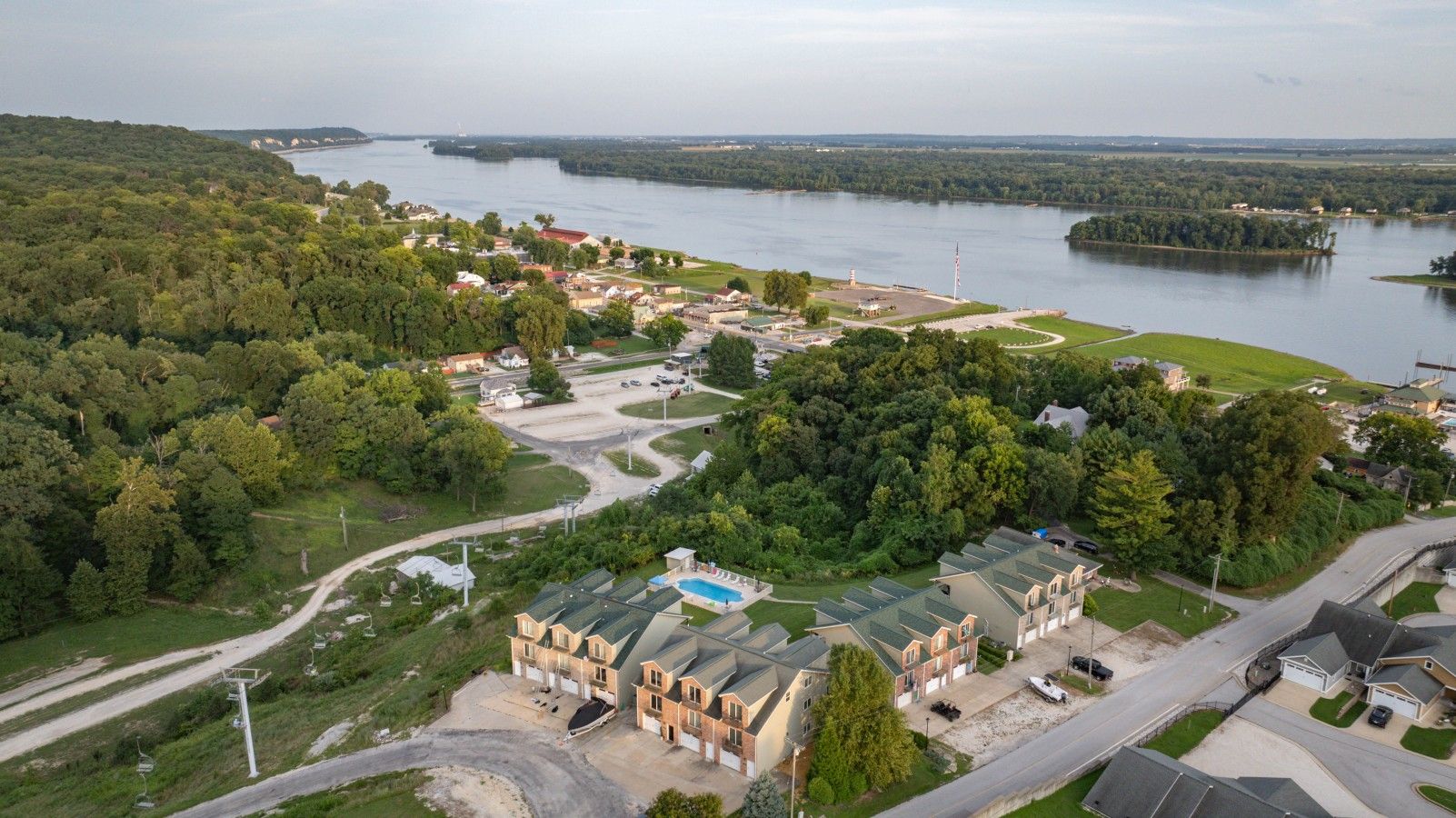 A residential area with a large building complex, a swimming pool, and a body of water in the background.
