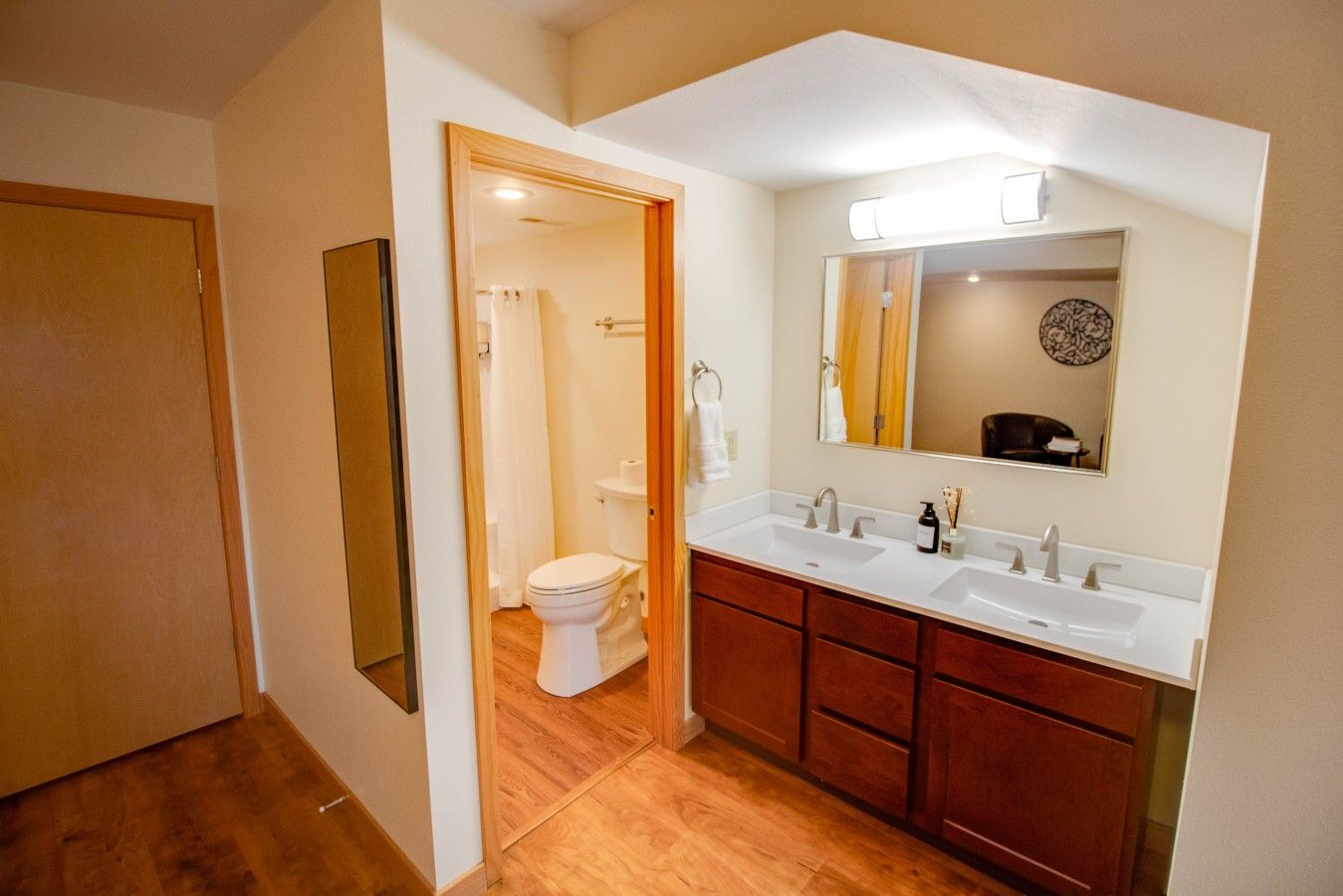 A bathroom with a double sink, a toilet, and a mirror.
