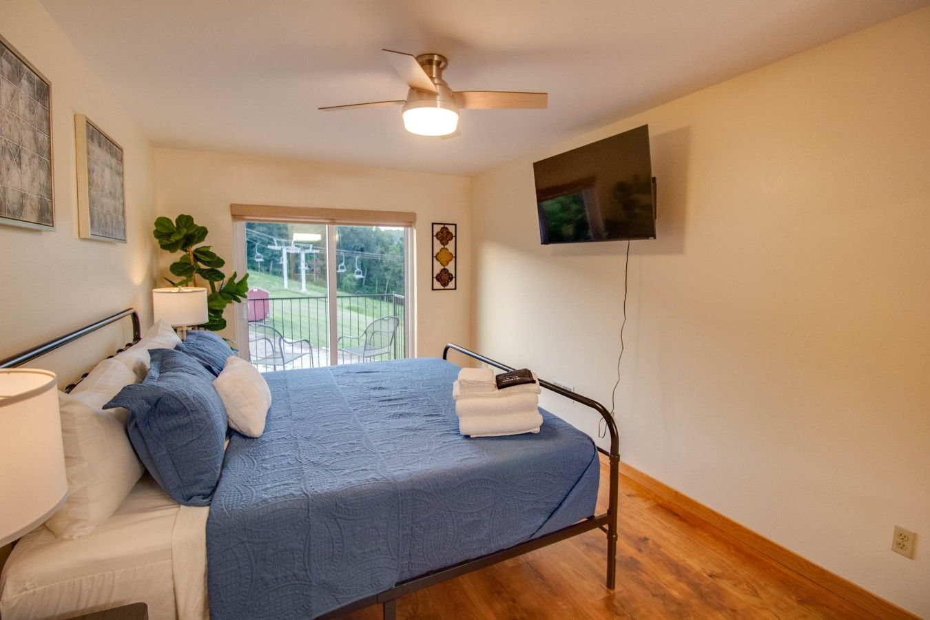 A bedroom with a bed, a ceiling fan, a TV, and a view of the outdoors.