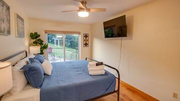 A bedroom with a bed, a ceiling fan, a TV, and a view of the outdoors.