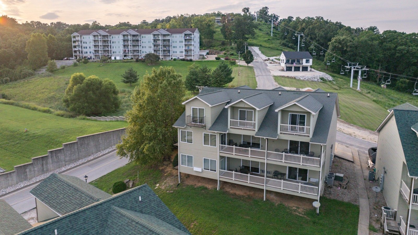 A multi-story building with balconies, a parking area, and a ski lift in the background.