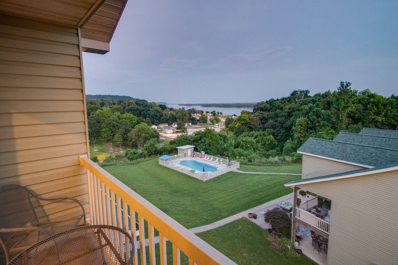 A residential property with a swimming pool, a balcony with a chair, and a view of a lake and surrounding greenery.
