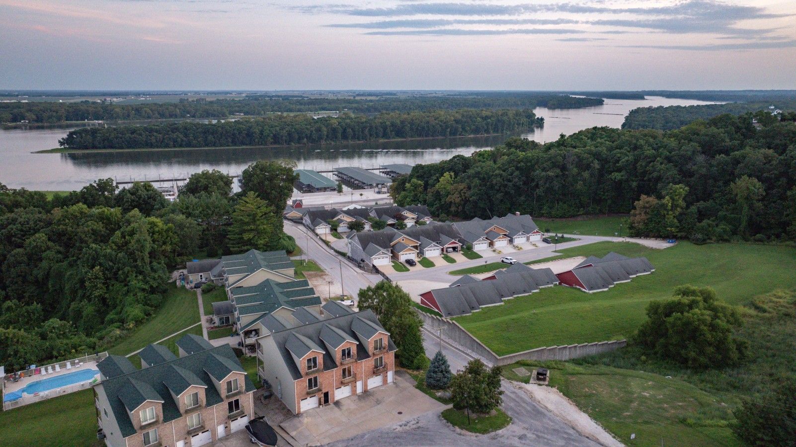 A residential area with houses, a swimming pool, and a large body of water in the background.