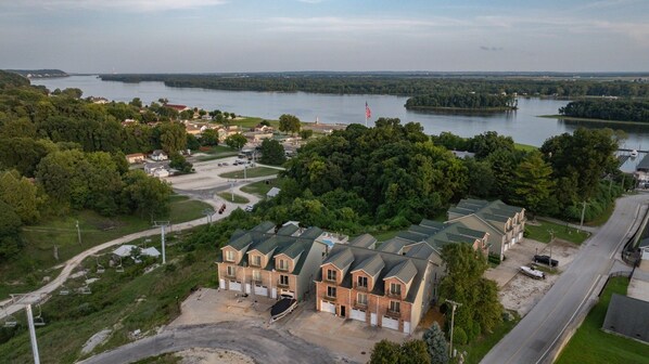 A residential area with a large building featuring a brick facade and multiple garage doors, surrounded by greenery and a body of water.