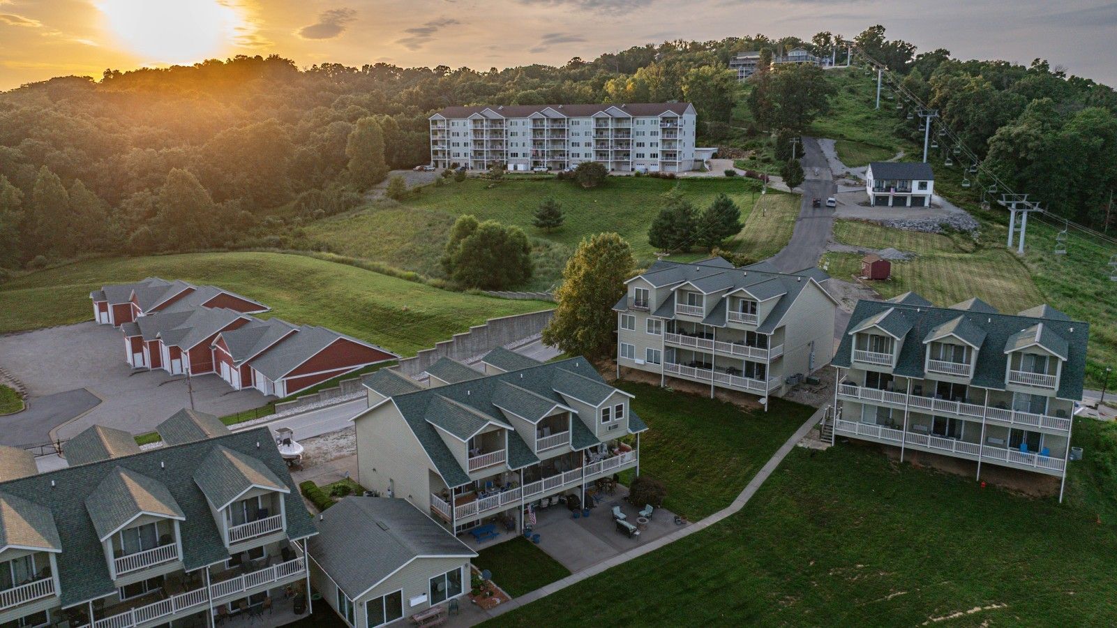 A residential area with multiple two-story houses, a central building with a balcony, and a hilly landscape in the background.