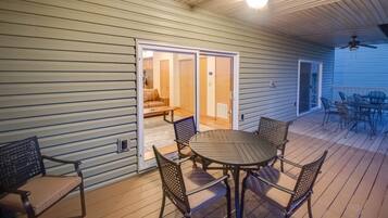 Een overdekt terras met een tafel en stoelen, een plafondventilator en uitzicht op een kamer met een schuifdeur.
