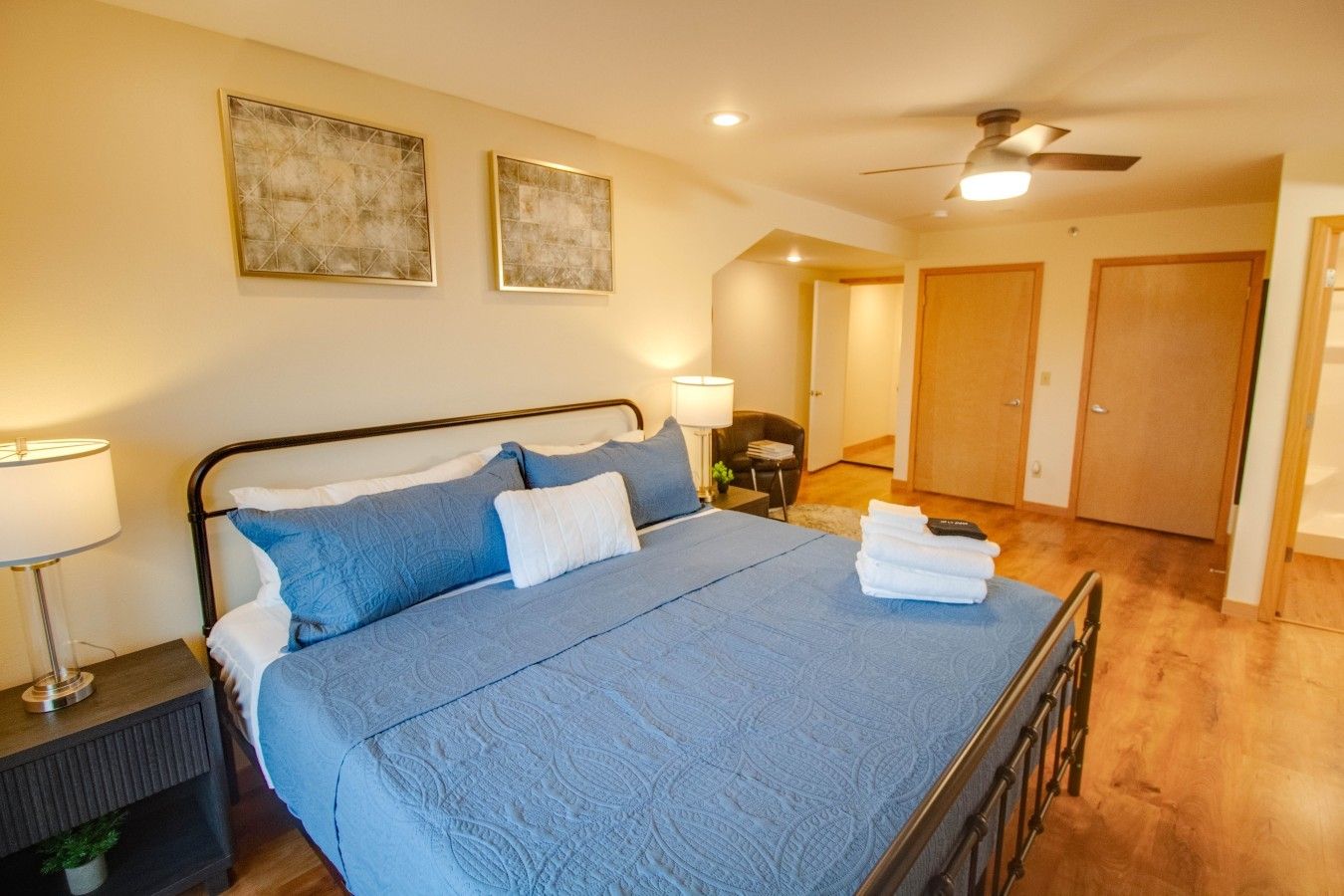 Een slaapkamer met een bed, nachtlampjes, een plafondventilator en een deur naar een andere kamer.