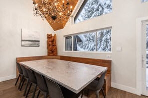 Ein Essbereich mit großem Tisch, Stühlen, einer Kandelaber, einem Fenster mit Schneeausblick und Kunstwerken an den Wänden.