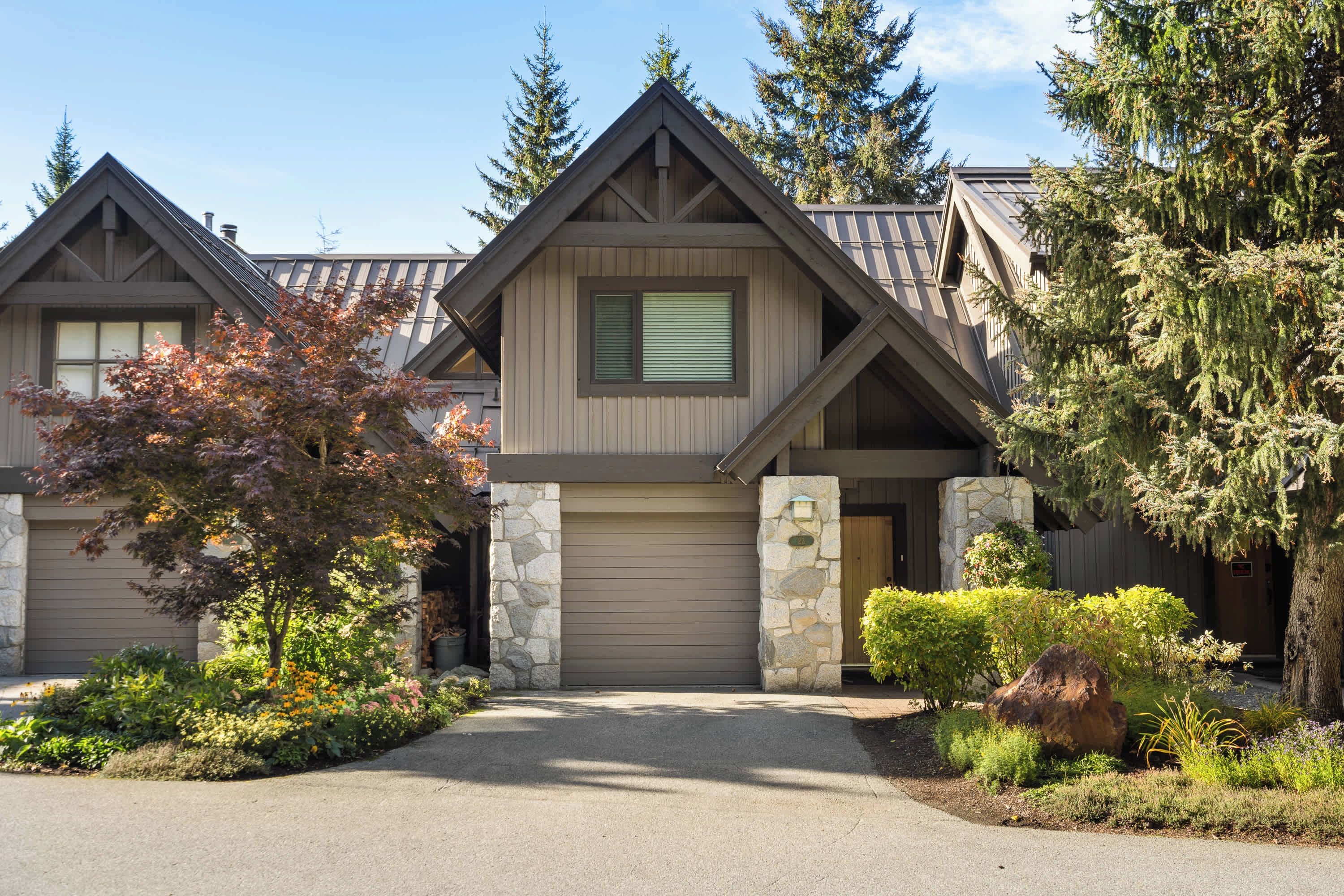 A two-story house with a stone foundation, a central garage, and a driveway leading to the entrance.