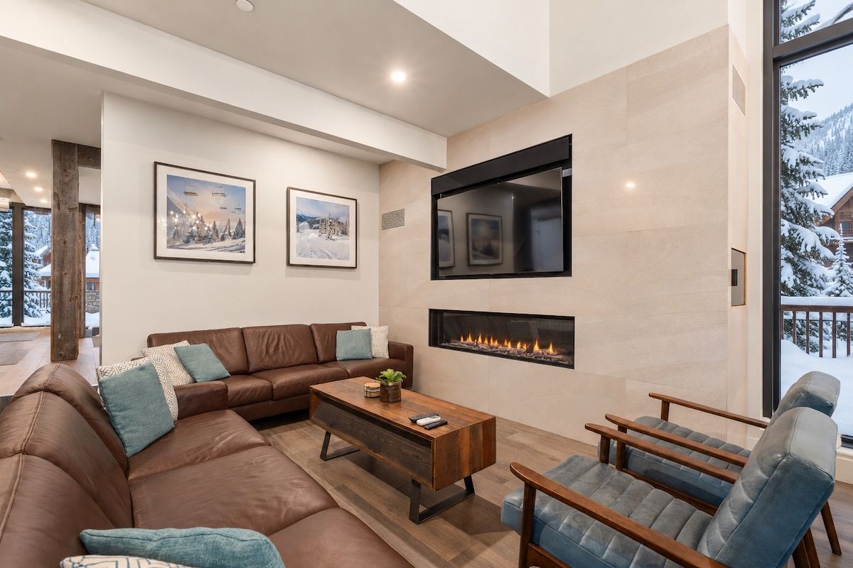 A modern living room with a fireplace, leather sofas, and a large window with a snowy view.