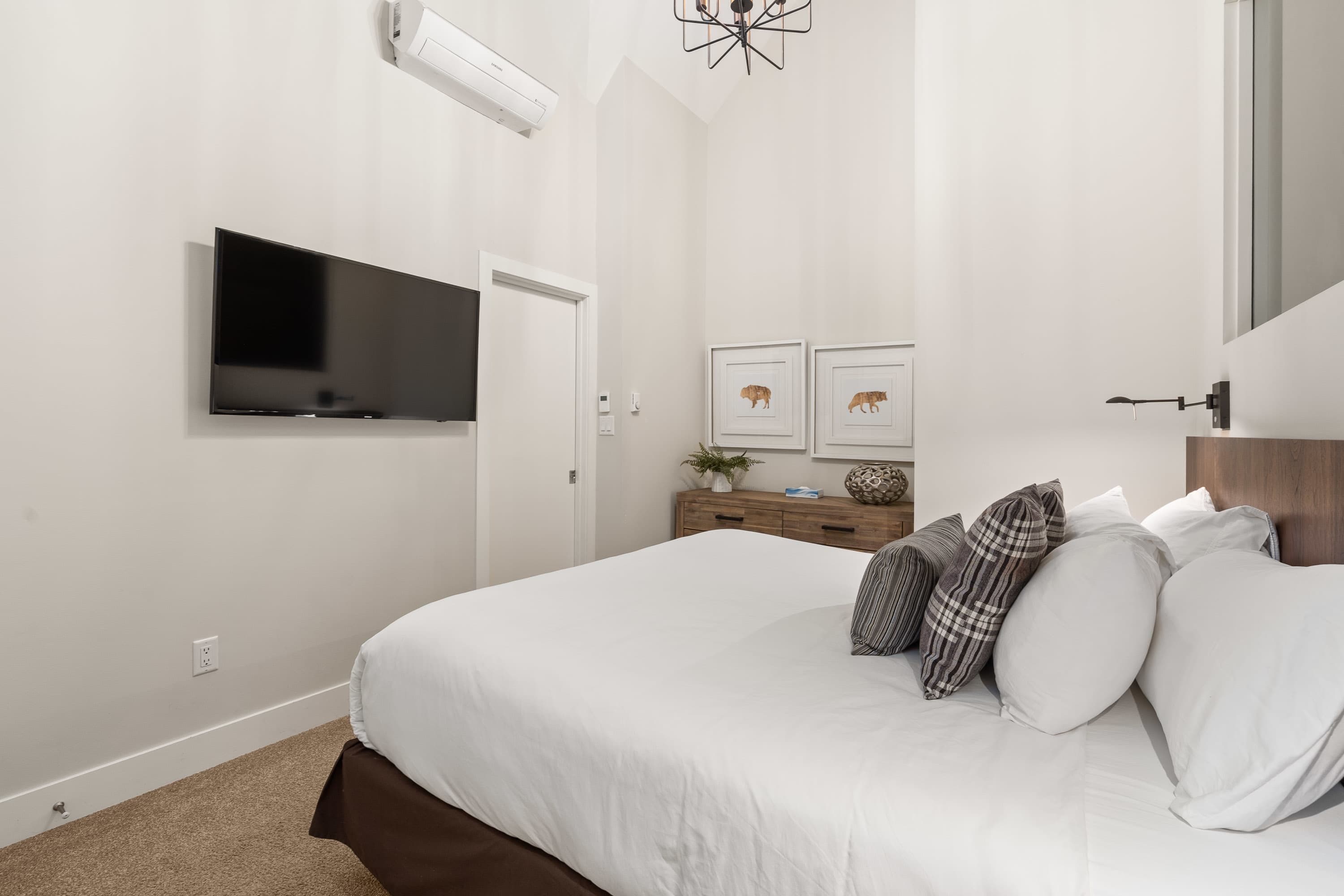 Ein Schlafzimmer mit einem Bett, einem an der Wand montierten Fernseher, einem Schminktisch und einem Spiegel.