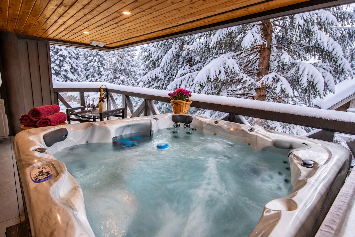 A hot tub with a wooden deck and a view of snow-covered trees.