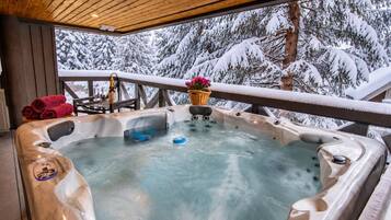 A hot tub with a wooden deck and a view of snow-covered trees.