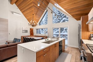 Eine moderne Küche mit einer zentralen Kochinsel, Holzschränken und großen Fenstern mit Blick auf schneebedeckte Bäume.