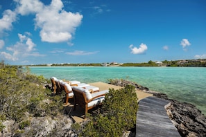 A beachfront property with a wooden deck and lounge chairs overlooking turquoise waters. - Secluded Oceanfront Villa | Direct Water Access (Providenciales)
