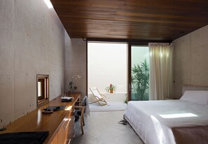 A modern bedroom with a wooden ceiling, a large bed, a desk with a chair, and a view of a balcony with plants. - Secluded Oceanfront Villa | Direct Water Access (Providenciales)