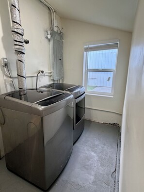 Een praktische keuken met een ingebouwde wasmachine en droger, een raam met uitzicht op een houten schutting en een zichtbaar stopcontact.
