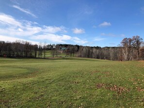 A grassy field with a building in the distance, surrounded by trees. - Villa 15 on Preserve Golf Course! (Pequot Lakes)