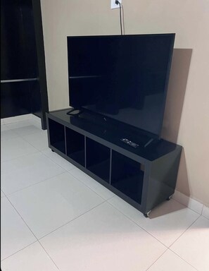 A black entertainment unit with a flat-screen TV, remote controls, and a power outlet. - Welcoming 2-bedroom apartment in vibrant Tijuana perfect for your stay (Tijuana)