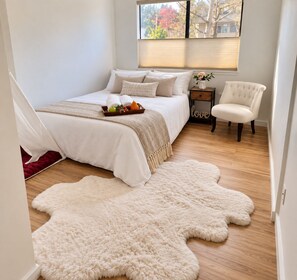 A bedroom with a bed, a chair, a window, and a rug. - Mercer Island Town Suites  (Mercer Island)