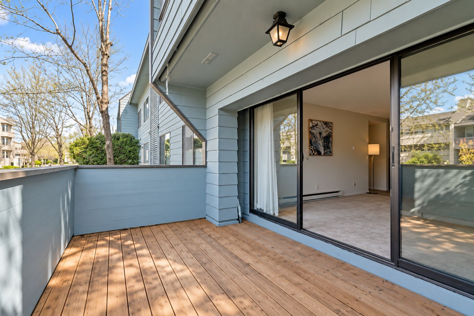 A balcony with a wooden floor, a sliding glass door leading to an interior room, and a view of the outside.