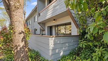 A modern two-story house with a balcony, surrounded by greenery and trees.