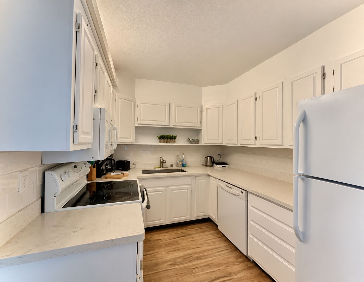 A modern kitchen with white cabinetry, a built-in oven, a dishwasher, and a refrigerator.