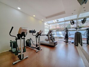 Un gimnasio con diverso equipo de ejercicio, ventanas amplias y suelo de baldosas.
