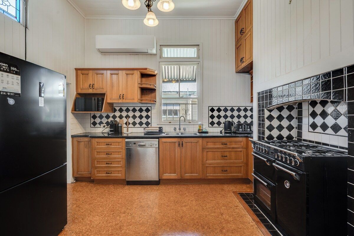 A kitchen with wooden cabinets, a black refrigerator, a dishwasher, a stove, and a window with blinds.