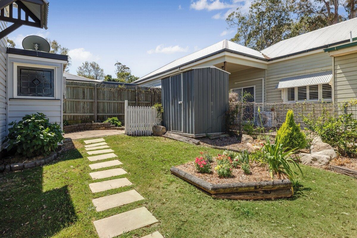 A residential property with a paved driveway, a fenced backyard, and a small shed.