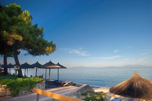 A beachside resort with thatched umbrellas, lounge chairs, and a view of the sea. - Portes Beach Hotel (Nea Propontida)