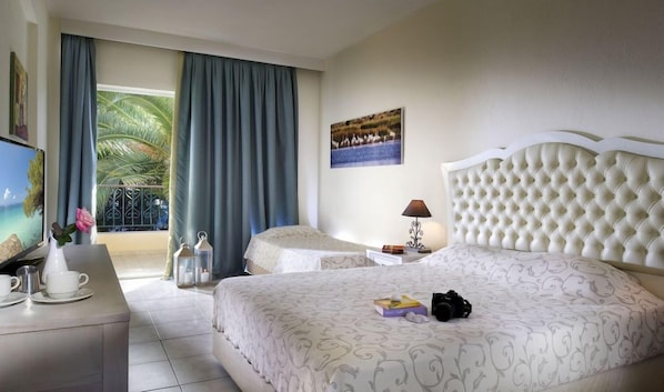 A hotel room with two beds, a TV, a balcony with curtains, and a painting on the wall. - Portes Beach Hotel (Nea Propontida)