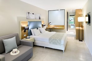 A modern hotel room with a bed, a sofa, a desk, and a TV. - Portes Beach Hotel (Nea Propontida)