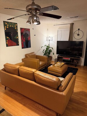 A living room with a brown leather sofa, a ceiling fan, a flat-screen TV, and a potted plant. - 3-bedroom house in delightful Decatur with cool AC breeze (Decatur)