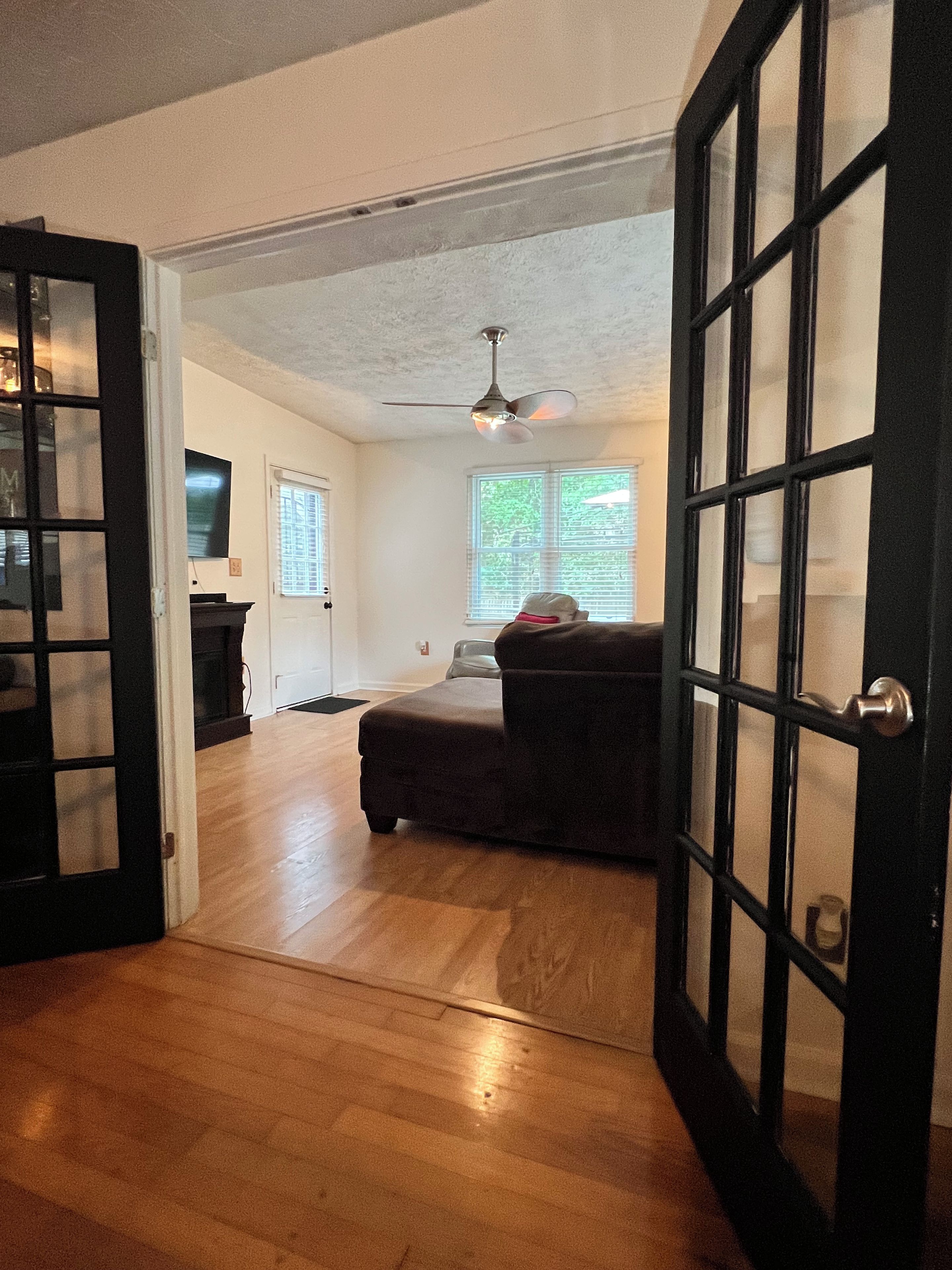An open doorway leading to a living room with a ceiling fan, a sofa, and a television.