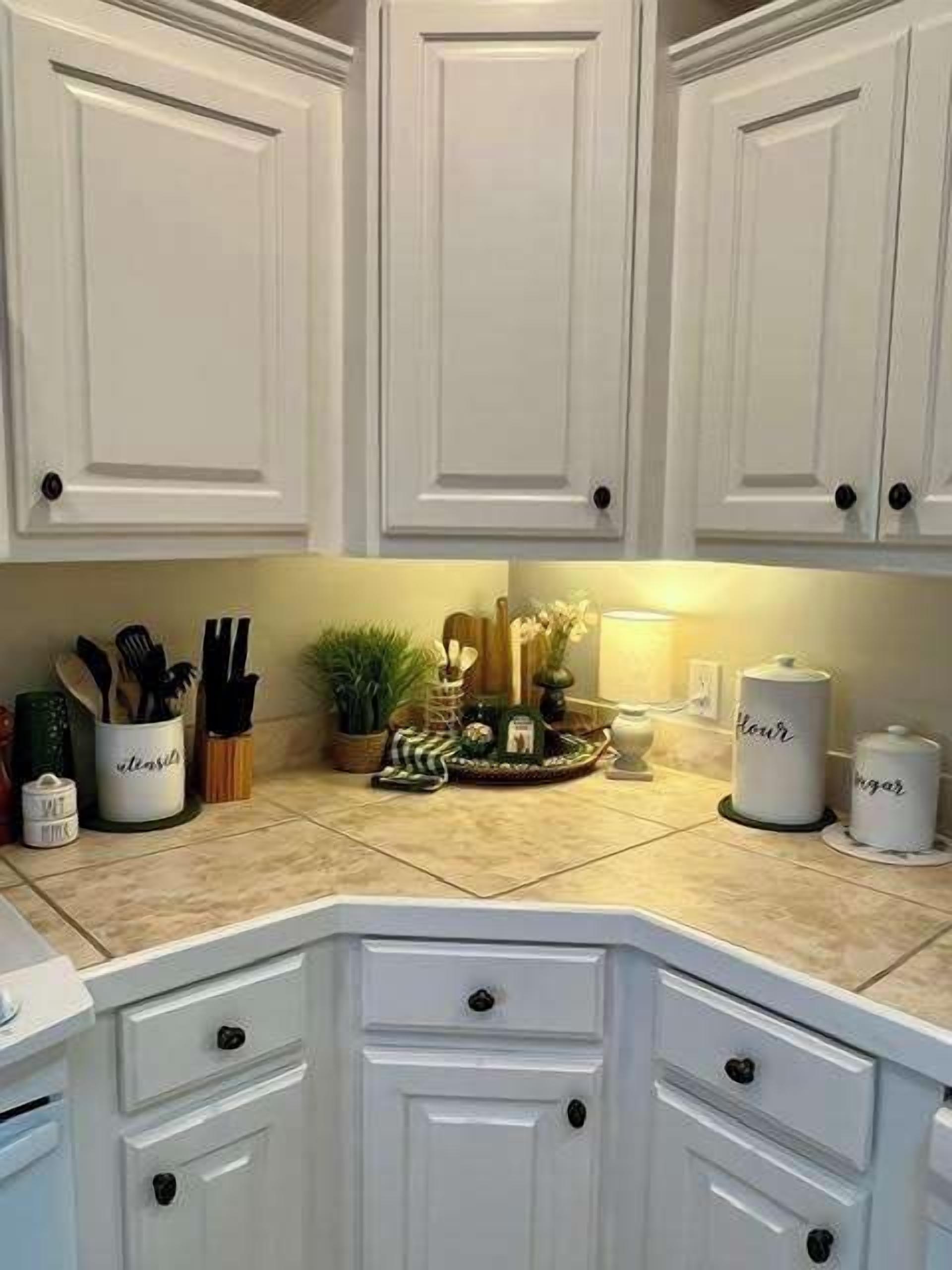 Una cocina con armarios blancos, una encimera con utensilios de cocina y una pequeña planta decorativa.