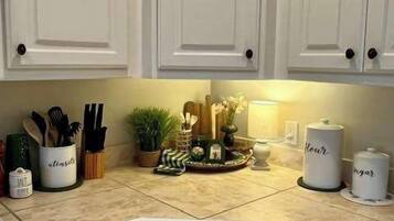 Una cocina con armarios blancos, una encimera con utensilios de cocina y una pequeña planta decorativa.