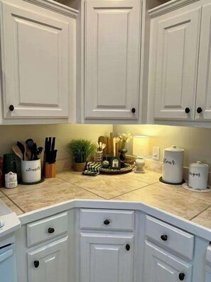 Una cocina con armarios blancos, una encimera con utensilios de cocina y una pequeña planta decorativa.