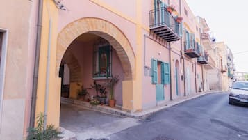 A street with a building featuring an arched entrance, potted plants, and a vehicle parked on the side.