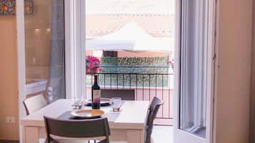 A dining area with a table set for two, a bottle of wine, and a view of a balcony with a white umbrella and greenery.