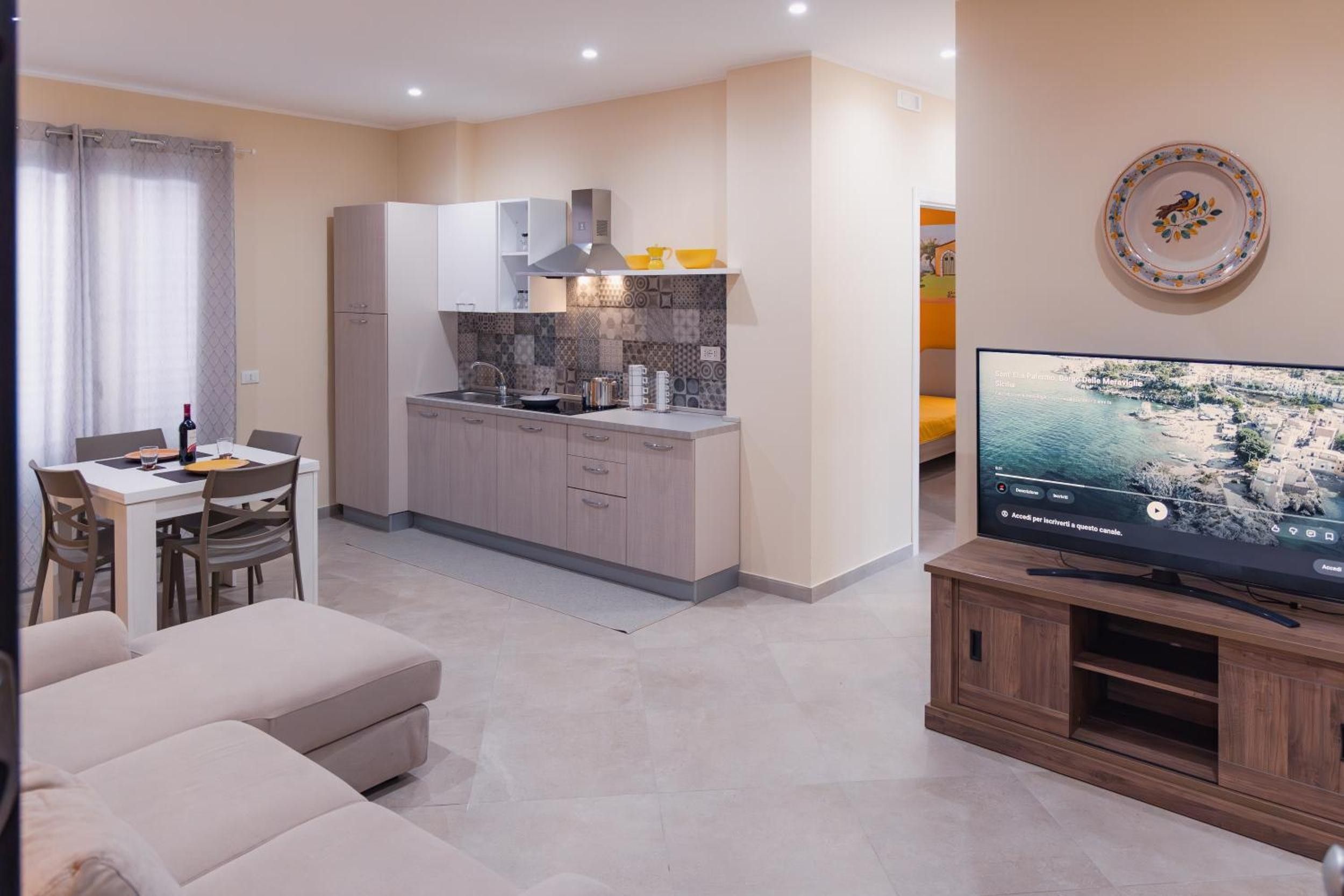 Ein modernes Wohnzimmer mit einem Flachbildfernseher, einem Essbereich mit Tisch und Stühlen sowie einer Küche mit Schränken und einer Arbeitsplatte.