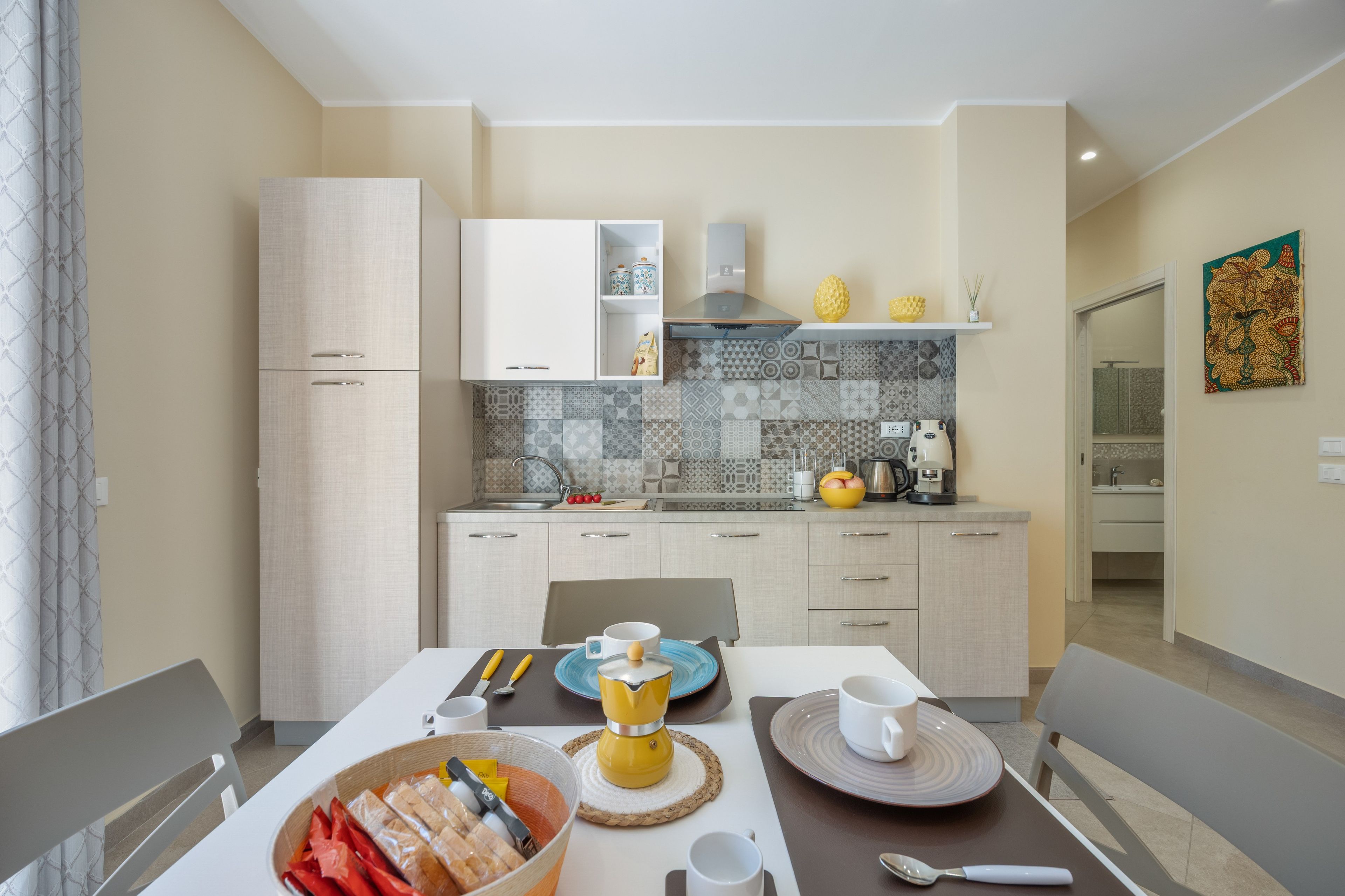 A modern kitchen with light-colored cabinets, a tiled backsplash, and a dining area with a table set for two.